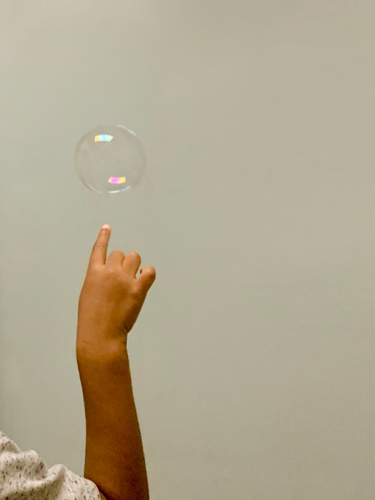 A child's hand reaches to pop a bubble.